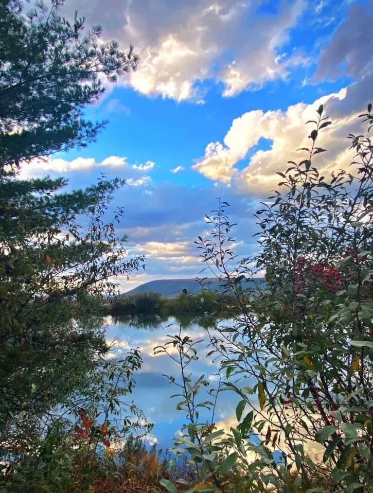 A calm Centre County pond reflecting an autumn sky, framed by trees and mountains.